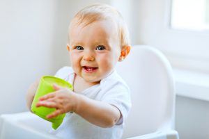 Cheerful baby girl sitting in chair and holding baby cup